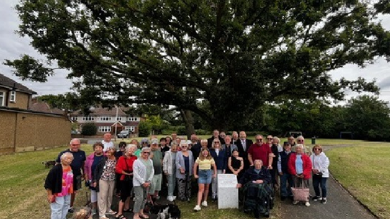 Group photo in front of white engraved village green plinth with large tree in background