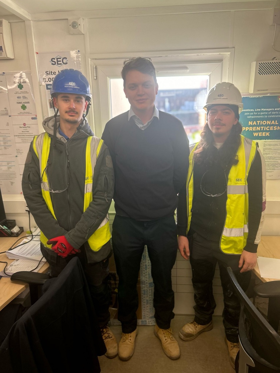 Image shows three men, two in protective kit (hard hat, high vis vest, gloves and hard boots) with their manager in the centre wearing a jumper and smiling