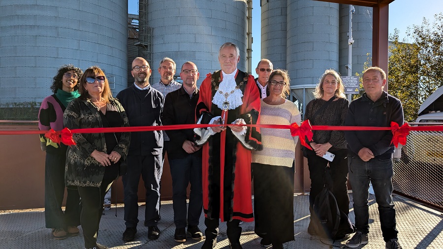 Mayor in ceremonial robes prepares to cut a red ribbon surrounded by smiling people