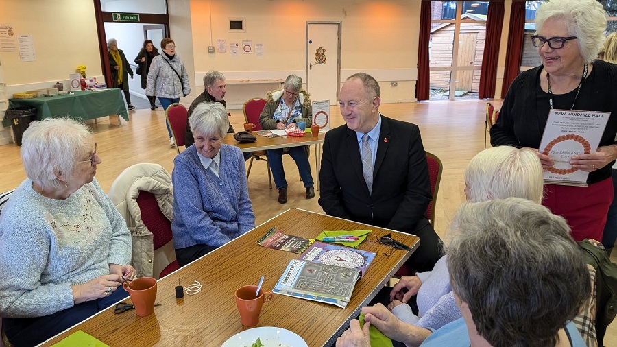 Image shows Leader of the Council, Councillor Ray Morgon seated at a table speaking to a group of smiling people